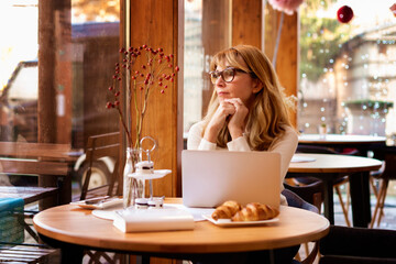 Business woman deep in thought while having breakfast and working on laptop in cafe. Small business.
