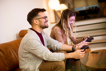Young couple playing video games at home, sitting on sofa and enjoying themselves