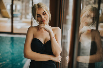 Beautiful young woman standing by the window at indoor swimming pool