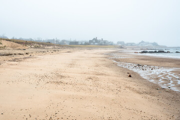 Empty sandy beach on a foggy autumn day. Oceanfront properties are visible in background. Sandwich, Cape Cod, MA, USA.