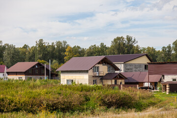 The roof of an old wooden house covered with sheets of brown metal tiles on a background of green coniferous trees on a summer day. Business selling building materials or helping low-income families.