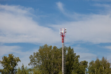Obraz premium A cell tower made of red-white metal in an inaccessible place in the Altai mountains against the background of green coniferous trees for transmitting a signal over radio waves for telephones.