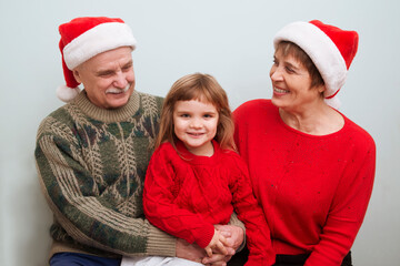 Grandparents  in a Santa's hat  
 embrace child granddaughter and celebrating holiday. Christmas time.