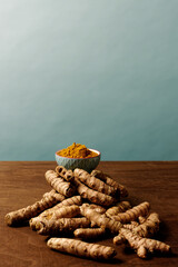 Turmeric unpeeled root and powder in blue bowl  at brown table. Blue background copy space above.