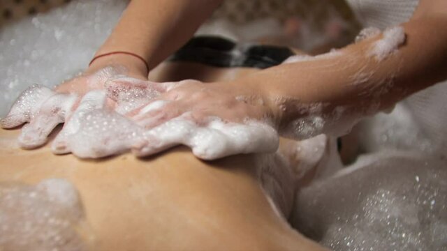 Woman masseur doing massage in hammam. Foam in the Turkish bath.
