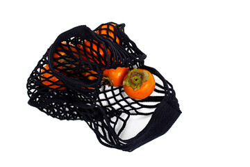 Black net bag with ripe orange persimmons isolated on a white background. Eco shopping concept.