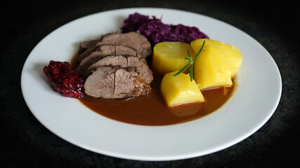delicious meal from a young chamois buck with potatoes and red cabbage, brown sauce and cranberries on a white plate