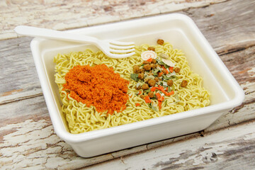 Instant dryed noodles with dry vegetables and spices with red pepper in disposable container with plastic fork. Traditional cheap Asian food. Fast food, raw noodles