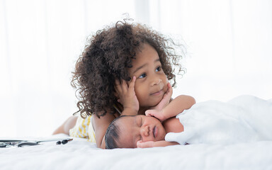 African girl looking at  her baby brother while sleeping on bed