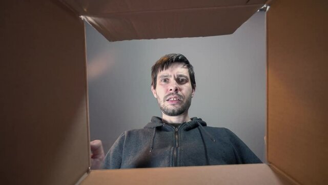 Young sad and disappointed man is opening gift and looking inside cardboard box.