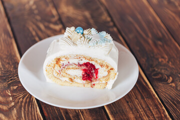Sliced piece from a roll cake of white color with cherry filling on against a wooden background. Christmas mood. Sweets for any occasion