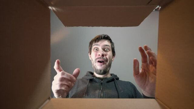 Young happy man is opening gift and looking inside cardboard box.