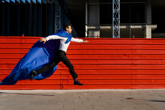 Businessman wearing superhero cape jumping on pavement in the city