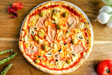 Quattro Staggioni pizza with olives, artichockes and ham served on a wooden table in trattoria italiana