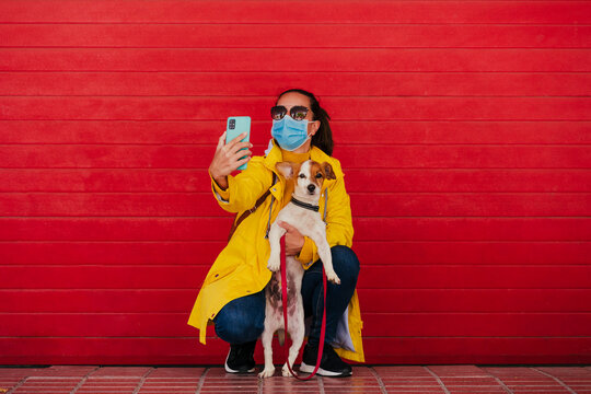 Woman with face mask and dog, taking smartphone selfies in front of red wall - Powered by Adobe