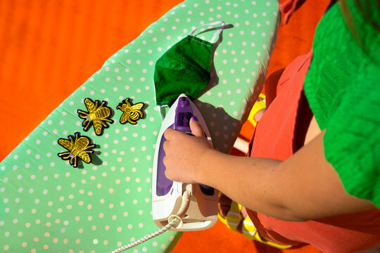 Teenage girl ironing bee patches on green protective mask