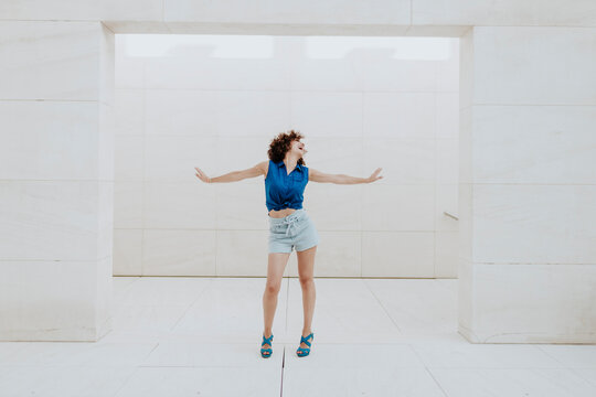 Carefree mid adult woman with arms outstretched standing against tiled wall