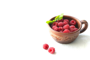 Raspberry fruits in a ceramic cup, healthy heap of summer berries on a white background.
