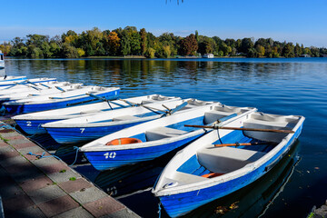 Fototapeta na wymiar Landscape with white and blue boats on Herastrau lake and large green trees in Herastrau Park in Bucharest, Romania, in a sunny autumn day.