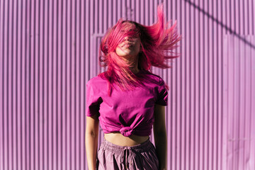Young woman with dyed red hair dancing in front of purple wall in the city