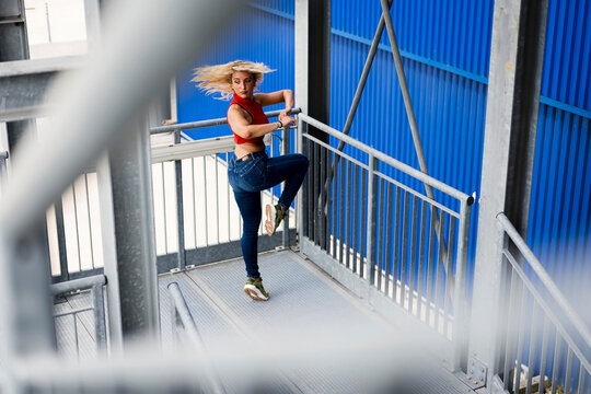 Young woman dancing by metal railing in front of blue wall in the city