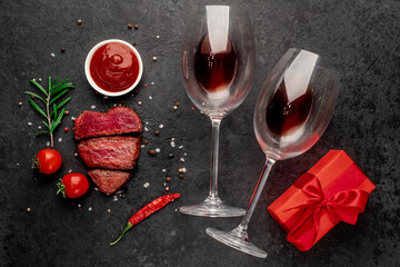 Dinner for two. Three pieces of meat. three types of roast meat, rare, medium, well done in the shape of a heart, two glasses of red wine and a gift on a stone background