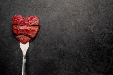 Different degrees of roasting beef steak in heart shape with spices on a meat fork on a stone...