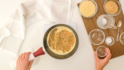 Chef cooking Alfredo sauce, close up view directly from above, white kitchen table background