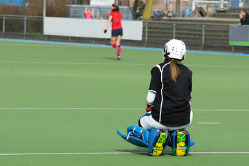 Field Hockey Goal Keeper, unrecognizable, with green playing field and in the distance player. Sports, champion.