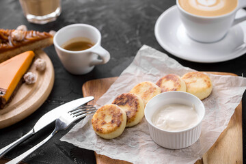 cottage cheese pancakes with sour cream sauce and cup of coffee on black table