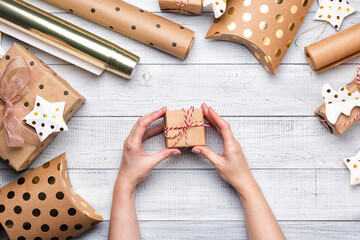 Christmas gift boxes and wrapping paper in gold colors on white wooden background. Copy space for your text. Flat lay and top view. Female hands