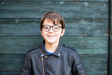 portrait of 11 year old boy with round glasses, leather jacket wood background
