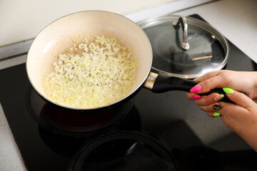 Female in a home kitchen fry the onions in a frying pan. Cooking dinner at home.