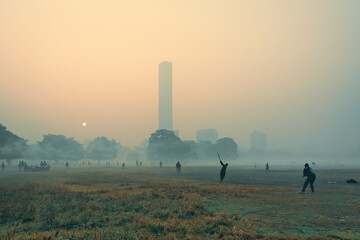 SIlhouette of young teenagers playing cricket surrounded by dense fog in a winter morning at...