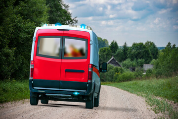 A red and white ambulance van speeding in the countryside gravel road with blue flasher lights on