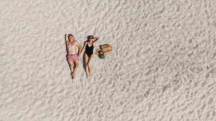 Aerial view of a young couple lying on the white beach sand. man and woman in swimwear spend time together and travel through the desert