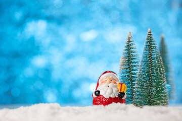 Winter background with Christmas trees and toy Santa Claus on a snow.