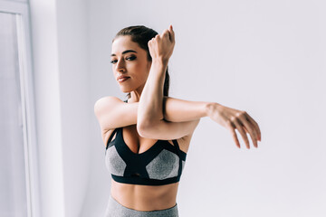 Young fitness woman exercising at home, stretching arms.