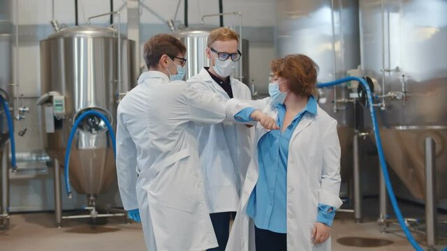 Factory workers wearing protective mask, gloves and lab coat greeting bumping elbows