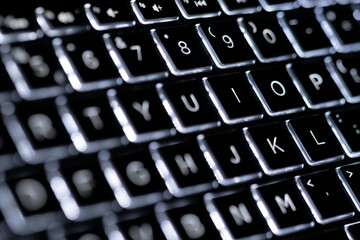 Illuminated, defocused laptop keyboard. Informatics background.