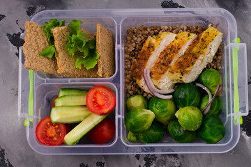 Healthy, diet food in boxes. Chicken fillet, buckwheat porridge, Brussels sprouts, tomatoes, cucumbers, bread. On a gray background. Top view