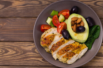 Healthy dietary salad with chicken fillet, avocado, nuts and fresh vegetables.Detox and healthy concept. Keto food. In a plate, on a wooden background.