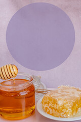 a woman's hand takes honey on a wooden stick from a full jar of honey with honeycombs on a plate