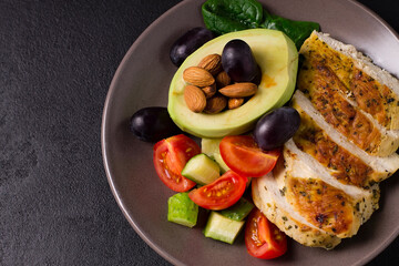 Healthy dietary salad with chicken fillet, avocado, nuts and fresh vegetables.Detox and healthy concept. Keto food. In a plate on a gray background.