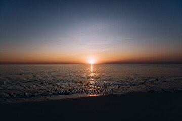 Breathtaking summer sunset view on the beach. Wonderful sunset landscape at the deep dark sea and orange sky above it and calm waves are flowing on it.