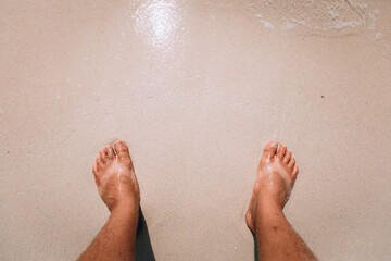 suntanned human feet with stripes of white skin from sandals in summer standing on the sand and sea...