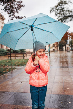 Little smiling happy girl holding big blue umbrella during walk on rainy gloomy autumn day