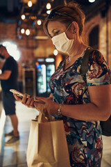 Young woman shopping in grocery store in the evening, wearing the face mask to avoid virus infection and to prevent the spread of disease in time of coronavirus