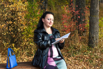 Fototapeta na wymiar happy pregnant brunette woman on a park bench in autumn reads a book.