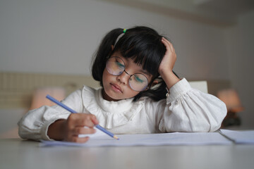 Naklejka na ściany i meble Asian little child girl wearing eyeglasses is doing a home work at home.